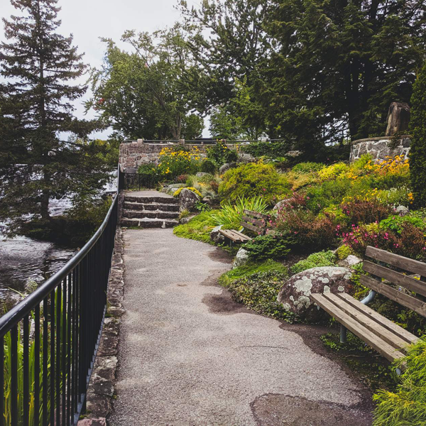 A paved path with a bench, railing, and steps near a body of water in a park